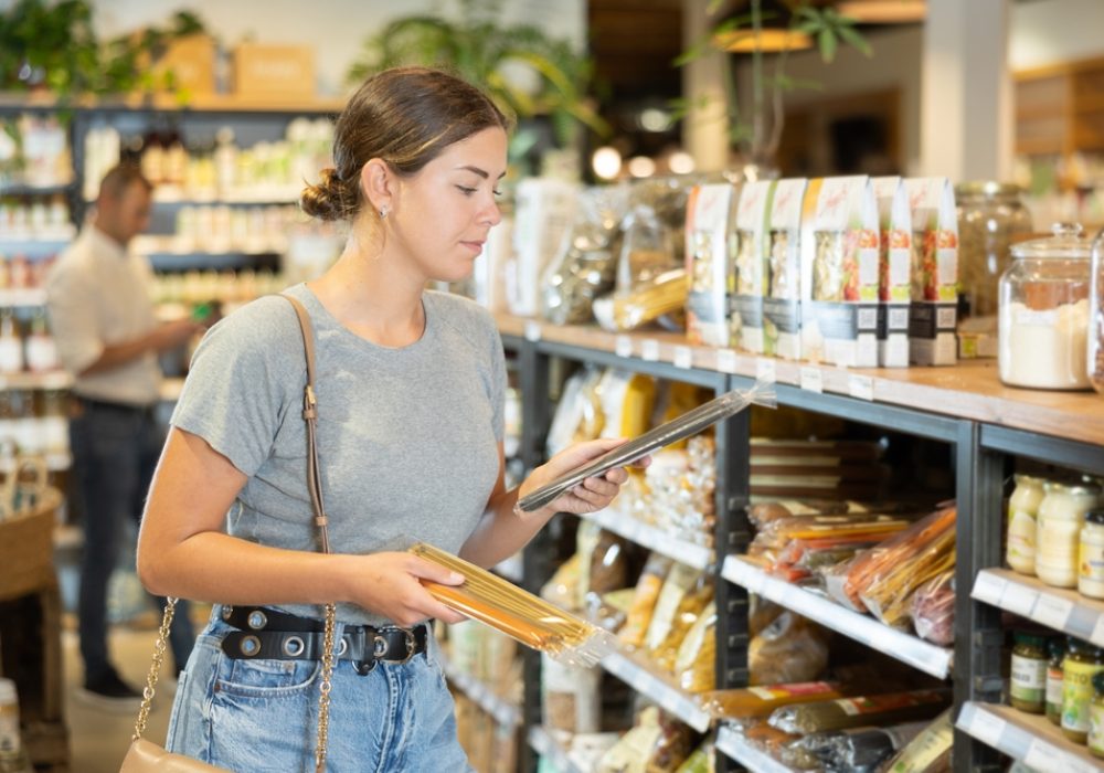 Interested,Young,Female,Shopper,Holding,Two,Different,Types,Of,Pasta,